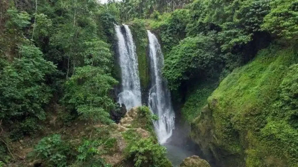 Air terjun kembar ini dikelilingi hutan tropis yang rindang, menciptakan suasana yang sejuk dan alami.